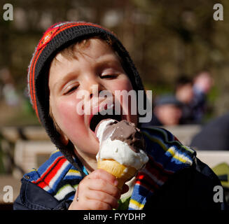 A four year old boy eating an ice cream - in springtime so he still has a hat on. Stock Photo
