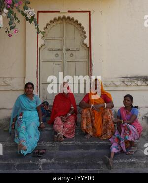A group of Indian women, wearing the typical bright saris of Rajasthan, each in a different colour, sit smiling on some steps. Stock Photo