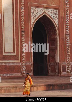 An Indian woman wearing a bright orange sari walks in front of Agra Fort near the Taj Mahal in Uttar Pradesh, India. Stock Photo