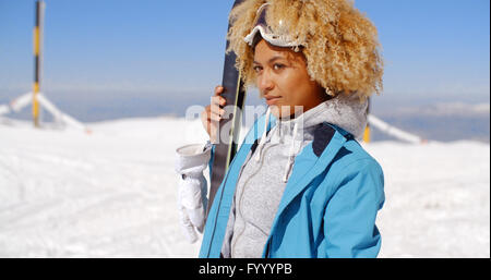 Thoughtful young woman standing holding her skis Stock Photo