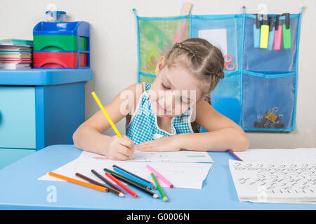 Happy five year old girl chose enthusiastically draws with colored pencils Stock Photo