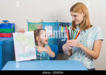 Five-year girl showing on the picture and looked at my mother who is holding in the hands of colored pencils Stock Photo