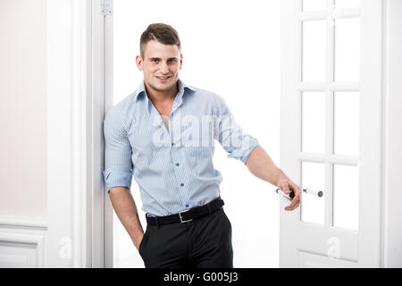 Portrait casual young man leaning against the frame of an open door on light background smiling and looking to camera Stock Photo