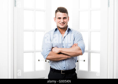 Portrait casual young man standing in the doorway home interior on light background smiling and looking to camera with hands folded Stock Photo