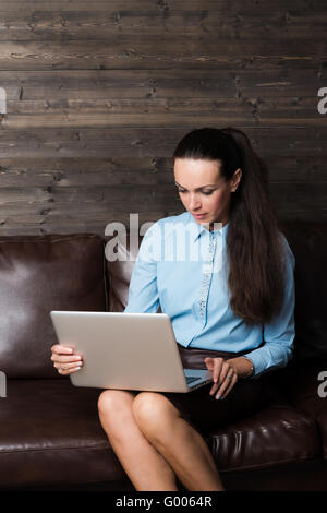 Happy brunette sitting on sofa in living room using laptop Stock Photo