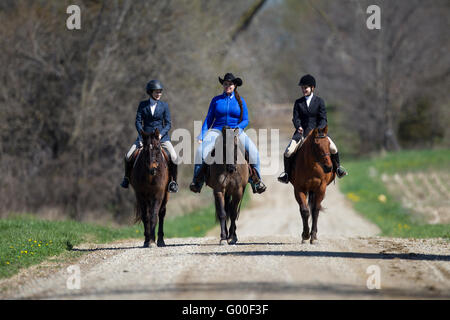 Three women riding horses together on a dirt road in the country. Stock Photo