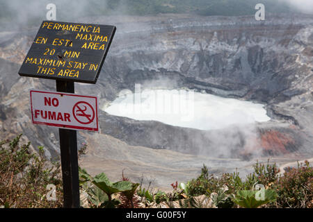 A sign warns visitors not to stay more than 20 minutes by the crater of Poas Volcano in Costa Rica. Stock Photo