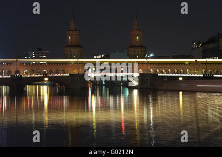 berlin oberbaumbrücke bridge at night with a passing metro train and a boat Stock Photo