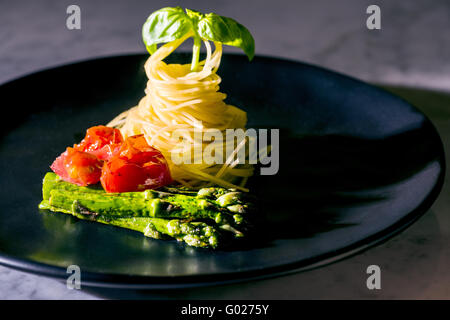 Pasta noodles spaghetti tomatoes basil asparagus on black plate green red black fine food italian italy classy fast modern kitch Stock Photo
