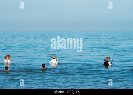 Three men standing in the sea fishing while two young boys are playing behind them. Stock Photo