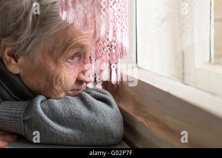 An elderly woman sadly looking out the window, face close-up. Stock Photo