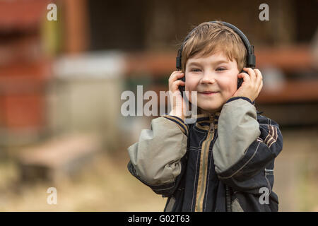 Little boy listening to music on headphones in the street, closeup portrait. Stock Photo