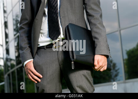 Unrecognizable businessman with suitcase close-up on a modern building background Stock Photo