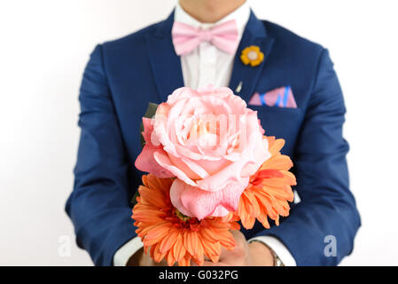 Man in blue suit with pink bow tie, flower brooch, and pink blue strip pocket square, close up, carry flowers Stock Photo