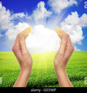 female hands holding sun over green field of grass and blue sky Stock Photo