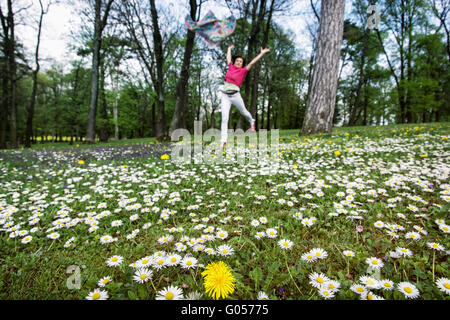 Young woman with silk scarf is jumping on the meadow full of ox-eye daisies and dandelions. Beauty, fashion and nature. Big fun.