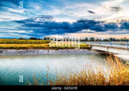 Bridge on large channel diverting river water for irrigation of cultivated fields Stock Photo