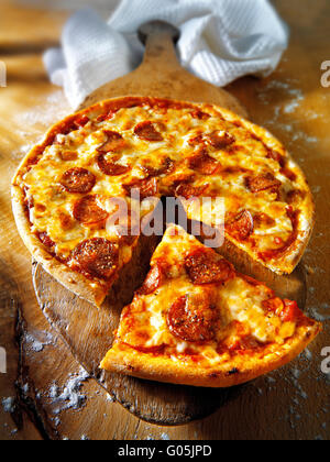 Cooked whole cheese and tomato pepperoni pizza with  a cut slice Stock Photo