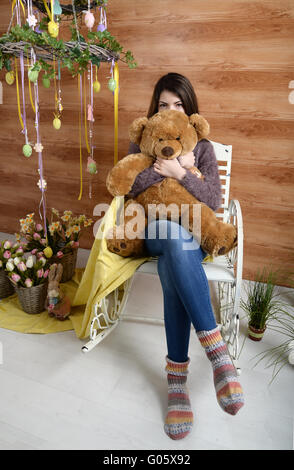 angry girl with a plush bear sitting on a chair Stock Photo