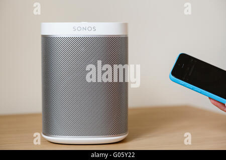 Person using an iPhone controller app to control music on a wireless digital speaker SONOS Play-1 loudspeaker on a table top at home. England UK Stock Photo