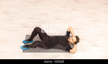 Bird eye view of a young man doing sit-ups on the floor in a gym. Stock Photo