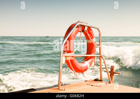 Bright red lifebuoy hanging on stern railings of fast safety rescue boat. Vintage tonal correction filter, photo with selective Stock Photo