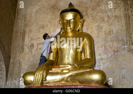 Man applies gold leaf to Buddha image, Burma Stock Photo