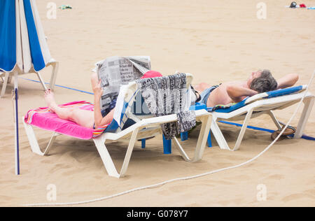 Glorious sunshine in Las Palmas, Gran Canaria, Canary Islands, Spain, 30th April 2016. Weather: cruise ship passenger reading English newspaper on sunlounger on city beach as cruise ship Emerald Princess ( passenger capacity over 3,000 ) makes its first port of call after departing from Southampton. Credit:  Alan Dawson News/Alamy Live News Stock Photo