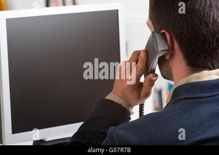 Casual Businessman Talking over the Phone and Looking at a Computer Screen Stock Photo