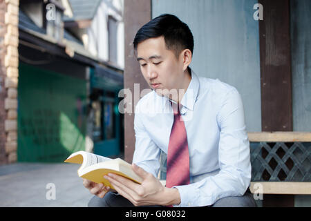 Asian Man Reading a Book Sitting on Bench Stock Photo