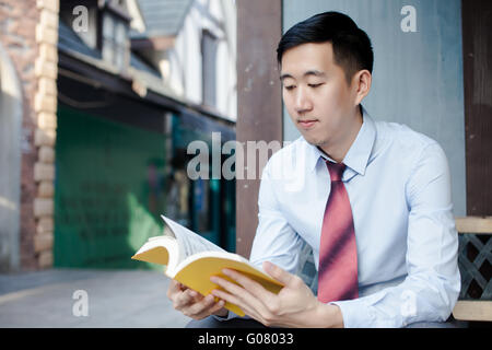 Asian Man Reading a Book Sitting on Bench Stock Photo