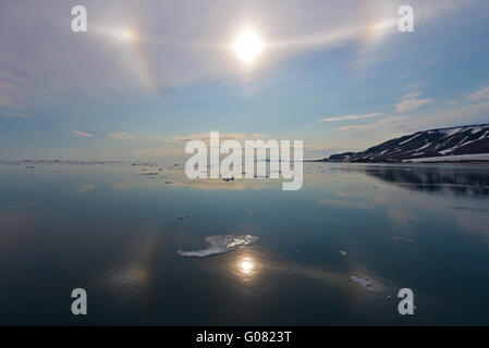 Parhelic circle and sun dogs in the sky and reflecting in the calm sea off Spitsbergen, Svalbard Stock Photo