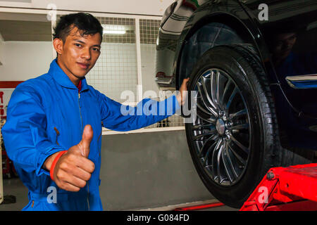 Happy young technician giving thumbs up while replacing tires. Stock Photo