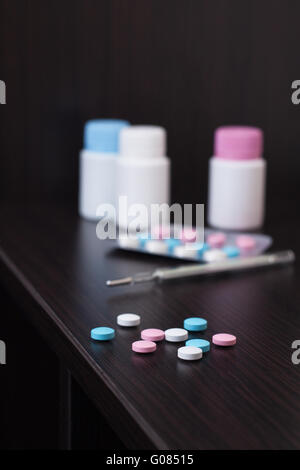 colorful pills and thermometer on brown table Stock Photo