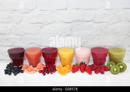 Fruit juice health drinks and smoothies with corresponding fruits against a white wall background. Stock Photo