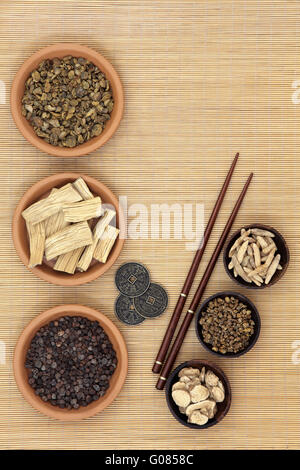 Traditional chinese herb ingredients used in alternative medicine, i ching coins and chopsticks over bamboo background. Stock Photo