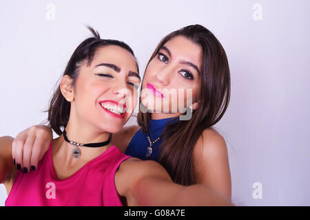 Two stylish women taking a selfie with a mobile phone. Best friends having fun, in urban outfit, isolated over grey background. Stock Photo