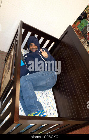 Proud black man age 23 testing comfort of crib for his new baby in showroom display. St Paul Minnesota MN USA Stock Photo