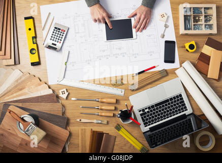 Construction engineer and architect's desk with house projects, laptop, tools and wood swatches top view, male hands using a dig Stock Photo