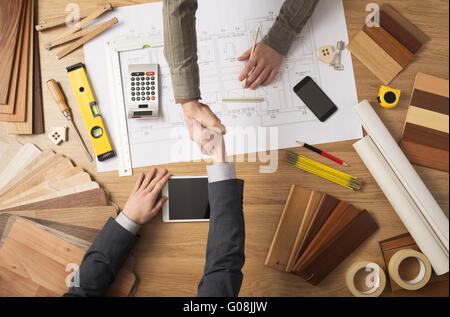 Architect and customer businessman shaking hands top view, desktop with building project, tools and wood swatches on background Stock Photo