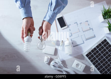 Man comparing an obsolete incandescent bulb and a CFL energy saving lamp, house project and solar panel Stock Photo