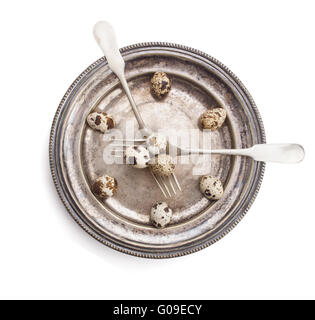 Clock made of quail eggs on silver plate with forks, isolated on white background Stock Photo
