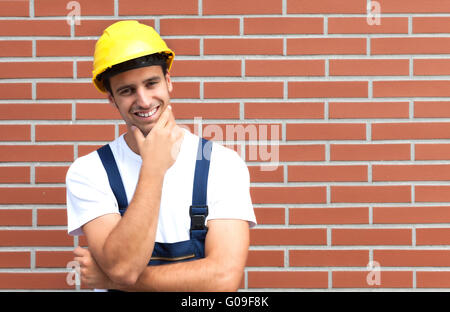 Thinking young worker in front of a brick wall Stock Photo