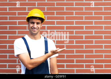 Presenting young worker in front of a brick wall Stock Photo