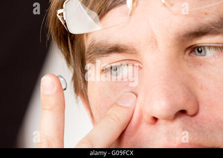 Closeup view of a man's brown eye while inserting a corrective contact lens on a finger. Stock Photo
