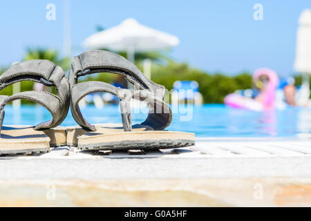 Leather sandals are on the edge of the swimming pool Stock Photo