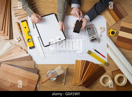 Business people working together on a building project, desktop top view with tools, wood swatches, mobile phone and blueprint Stock Photo