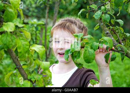 The girl winks one eye against spring foliage Stock Photo