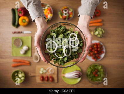Hands holding an healthy fresh vegetarian salad in a bowl, fresh raw vegetables on background, top view Stock Photo