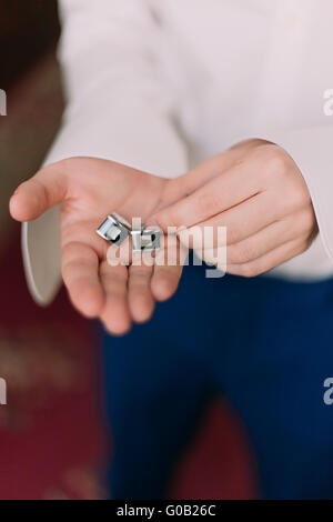 Closeup of handsome man in white shirt and blue suit holding the cuff links his hand Stock Photo